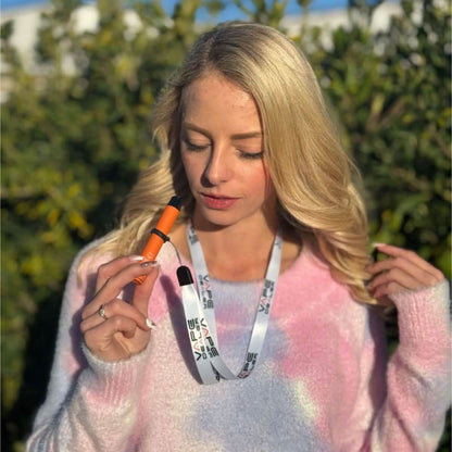 Frau trägt ein Vape Lanyard in Weiß, hält eine orangefarbene E-Zigarette und genießt den sonnigen Tag.